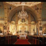 East wall and apse of Ukrainian Catholic Church with detailed wall art and red carpet between pews