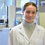 Student in a white lab coat standing in a chemistry lab.