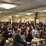 Audience sitting on chairs in a large room paying attention to the presenter.