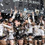 "University of Manitoba Bisons women’s volleyball team celebrates their 2025 U SPORTS National Championship victory. Players, wearing championship hats and medals, cheer and raise the championship trophy high as gold, black, and white confetti rains down. A University of Manitoba and Bisons-branded banner hangs in the background, highlighting the team’s triumphant moment.