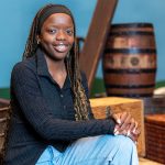 A student is sitting on a stage in front of a series of wooden boxes and barrels.
