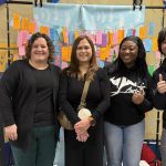 Four people standing in a hallway in front of a rack full paper tabs, smiling for a photo.