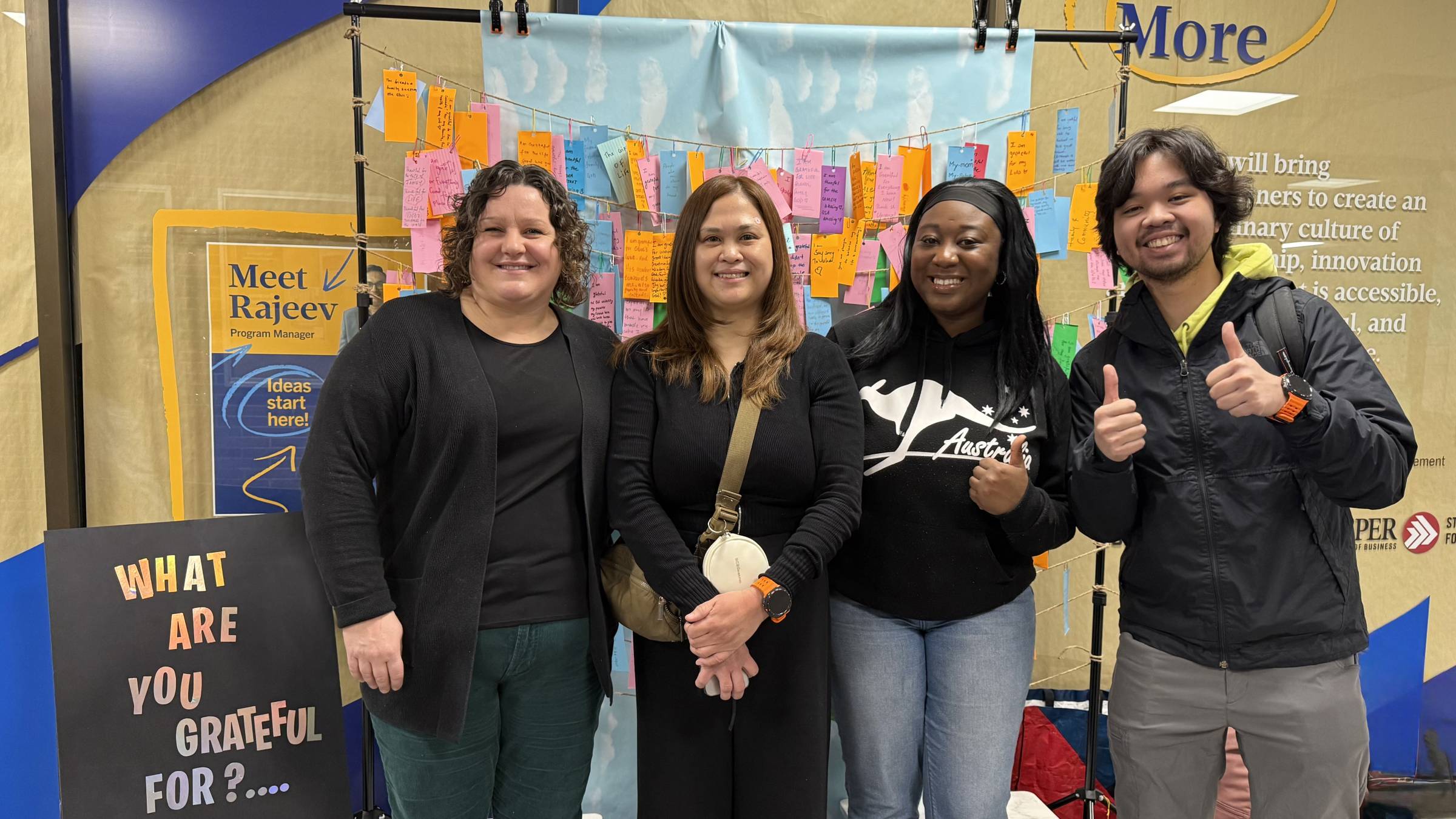 Four people standing in a hallway in front of a rack full paper tabs, smiling for a photo.