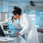 A researcher looks into a microscope in a biomedical lab.