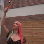 student reaches for copper jingle with cedar plaque displayed behind her