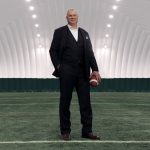 Randy Ambrosie, Commissioner of the CFL, stands on green turf holding a football