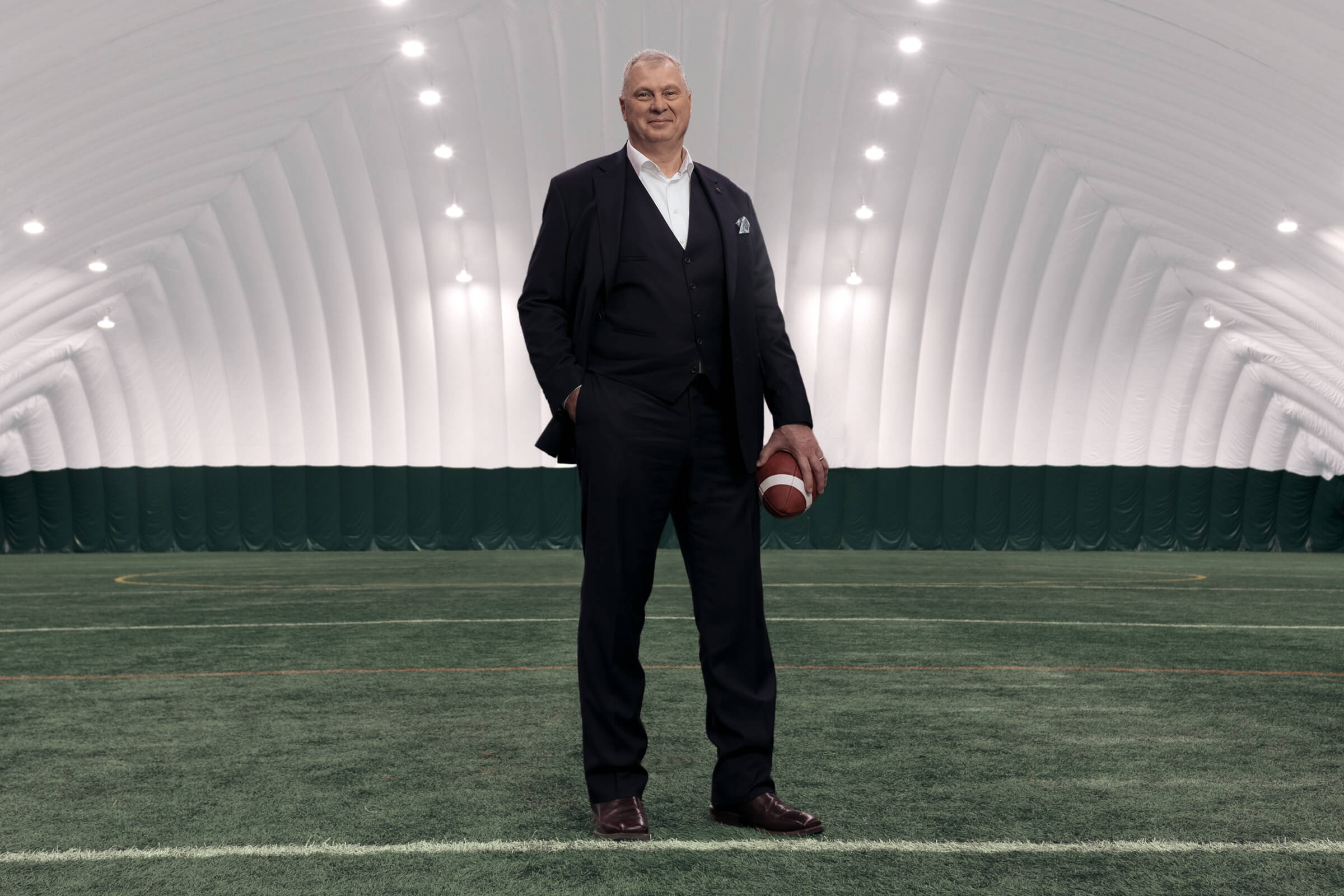 Randy Ambrosie, Commissioner of the CFL, stands on green turf holding a football