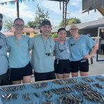 Five dental students pose for a photo. Dozens of dental instruments are laid out on a table in front of them. A Canadian flag is in the background and a sign that reads "Kindness in Action."