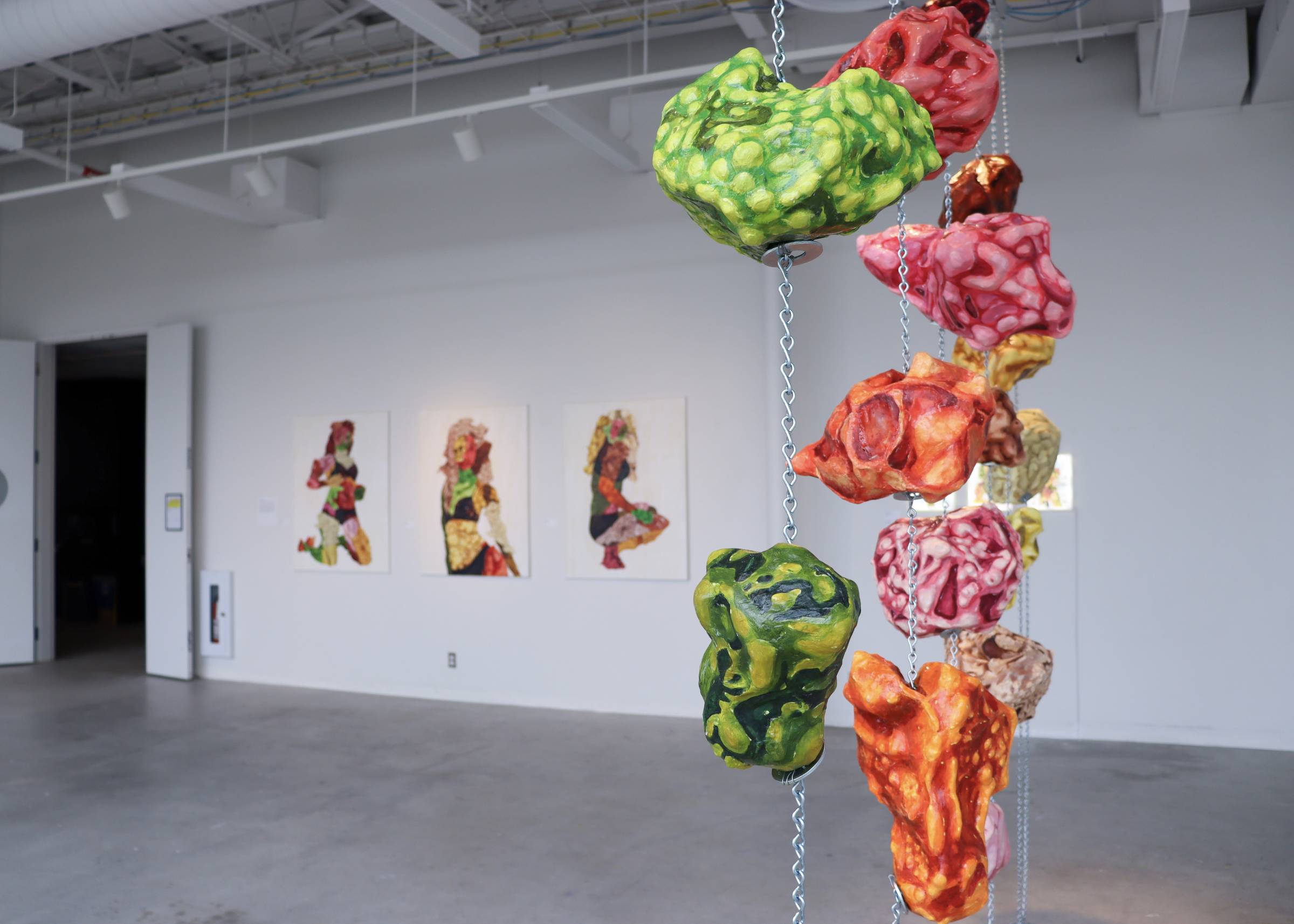 Colorful hanging sculptures and bold figure paintings installed in a contemporary gallery space at the School of Art, University of Manitoba.
