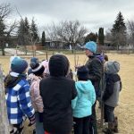 PromoScience instructor stands outside with students of Ecole Crane delivering STEM teachings through an Indigenous lens.