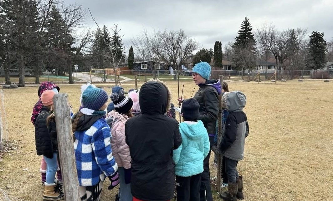 PromoScience instructor stands outside with students of Ecole Crane delivering STEM teachings through an Indigenous lens.