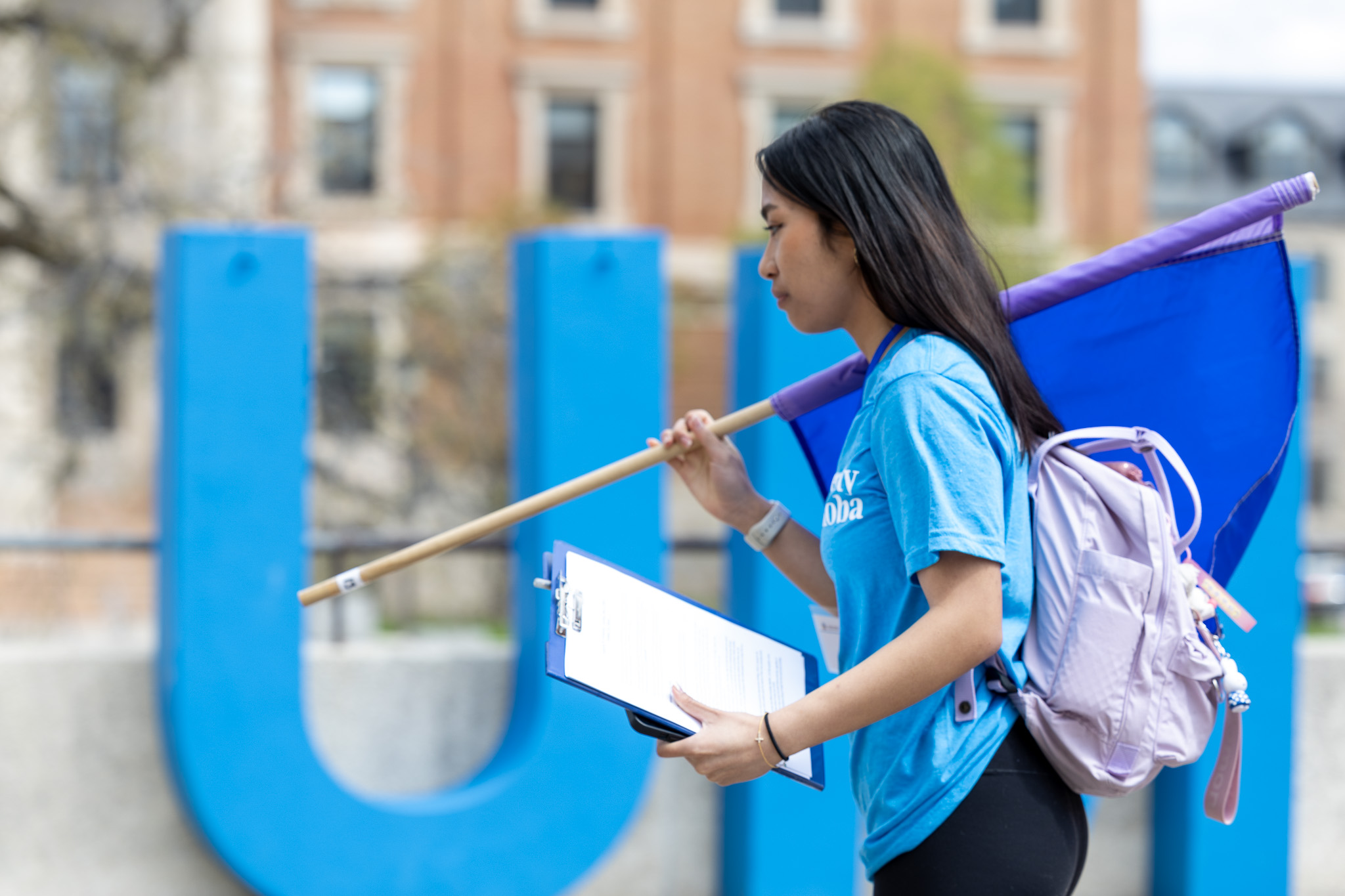 2024 Preparing for University orietation volunteer with a flag infront of the blue UM letters and the admin buiding in the foreground