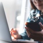 Woman working on a laptop computer and using a mobile phone.