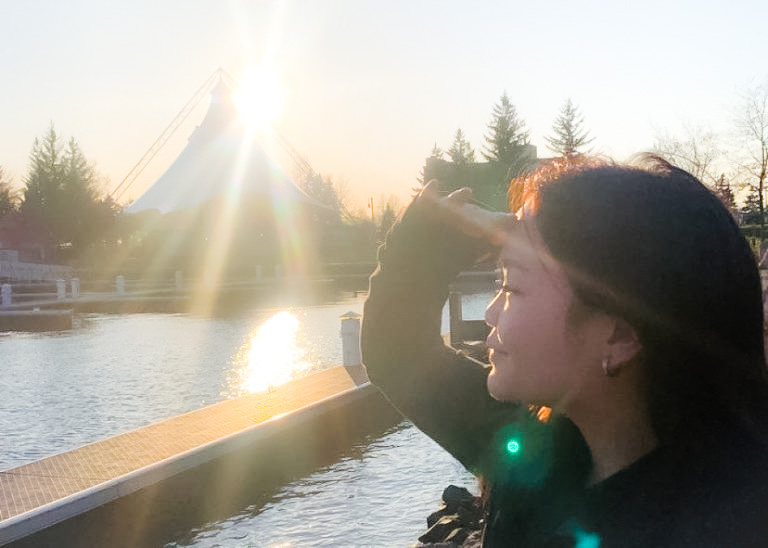 A person looking out over a body of water with a sunset behind a large tent in the background.