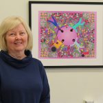 Gayle Restall stands in front of artwork that depicts the importance of collaborative relationships in occupational therapy.