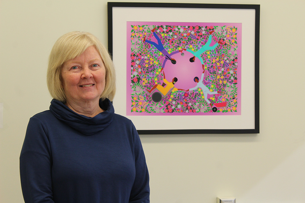 Gayle Restall stands in front of artwork that depicts the importance of collaborative relationships in occupational therapy.