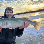 Holding a big fish by the sun on the horizon over the lake in winter