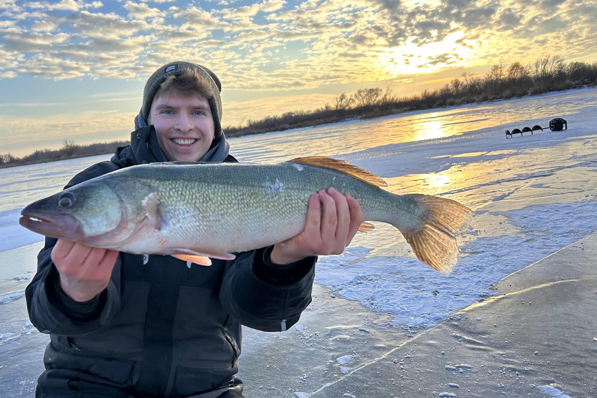 Holding a big fish by the sun on the horizon over the lake in winter