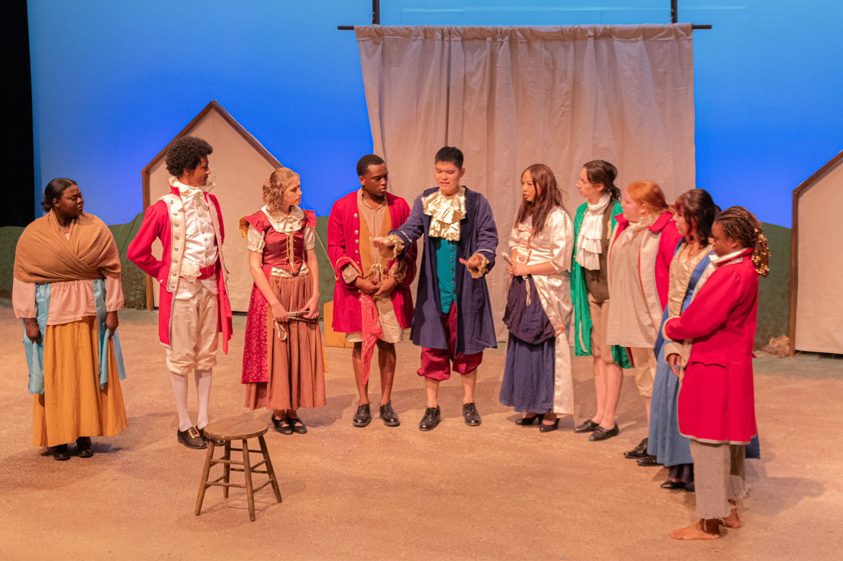 A group of ten actors on stage, dressed in colonial costumes, standing in a semi circle.