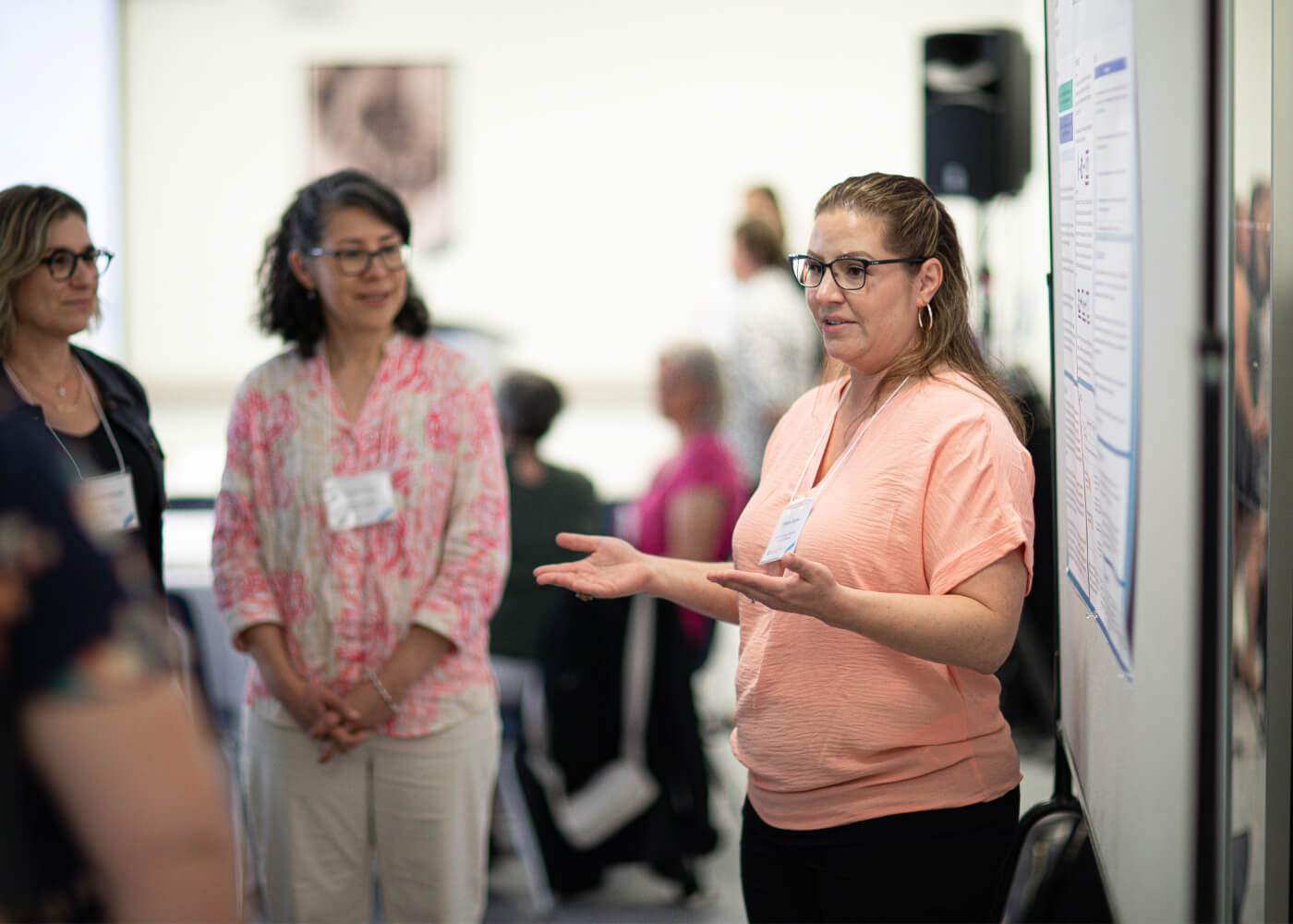 Instructor presents her research, standing in front of a poster display.