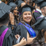 A group of grads in black caps and gowns and colourful stoles smile excitedly on Convocation day