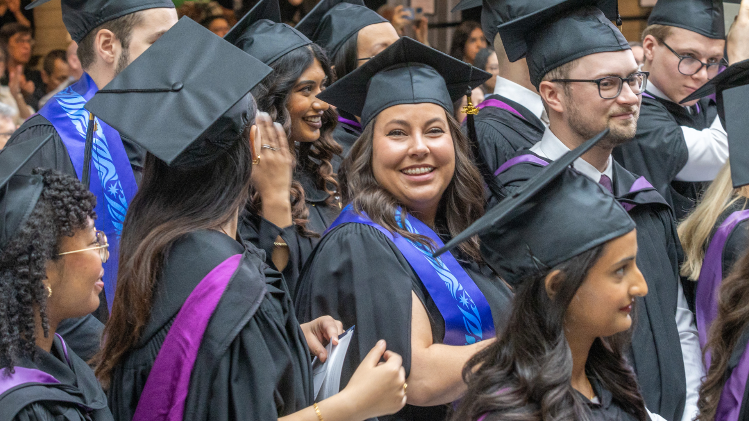 A group of grads in black caps and gowns and colourful stoles smile excitedly on Convocation day