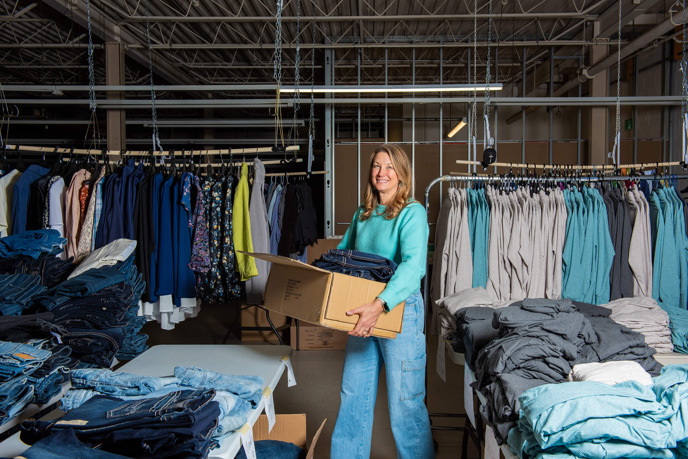Kristie Pearson holding a box of clothes in a warehouse while looking at the camera