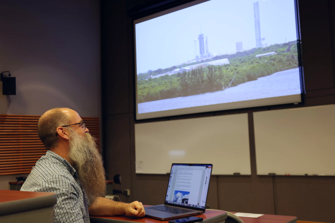 A person in front of a laptop looking at a large projector screen