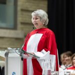 Sister Lesley Sacouman speaks at Convocation, wearing a red and white ceremonial gown.