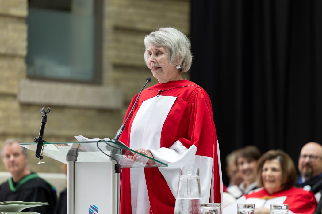 Sister Lesley Sacouman speaks at Convocation, wearing a red and white ceremonial gown.