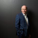 Incoming Chancellor Dave Angus stands against a dark wall, looking off to the side