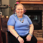Alumna Sandy Hyman smiles while sitting in front of a fireplace