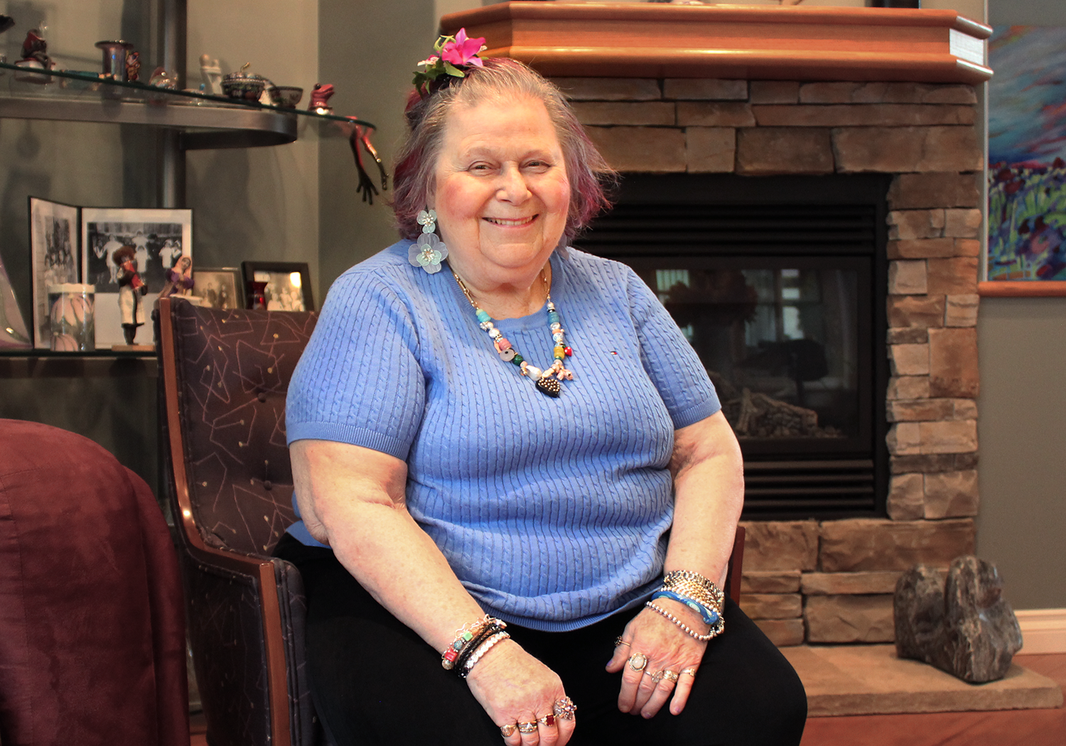 Alumna Sandy Hyman smiles while sitting in front of a fireplace