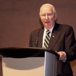 Dr. Henry Friesen speaks at a lectern.