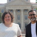 Two people smiling in front of the administration building.