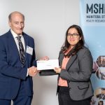 A person presenting an award to a student, behind them there's a banner that says MSHRF - Manitoba Student Health Research Forum, Celebrating Excellence in health research.