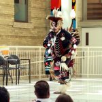 Dancer is wearing regalia adorned with beads, feathers and embroidery.