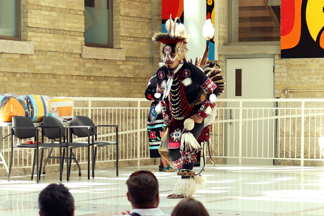 Dancer is wearing regalia adorned with beads, feathers and embroidery.