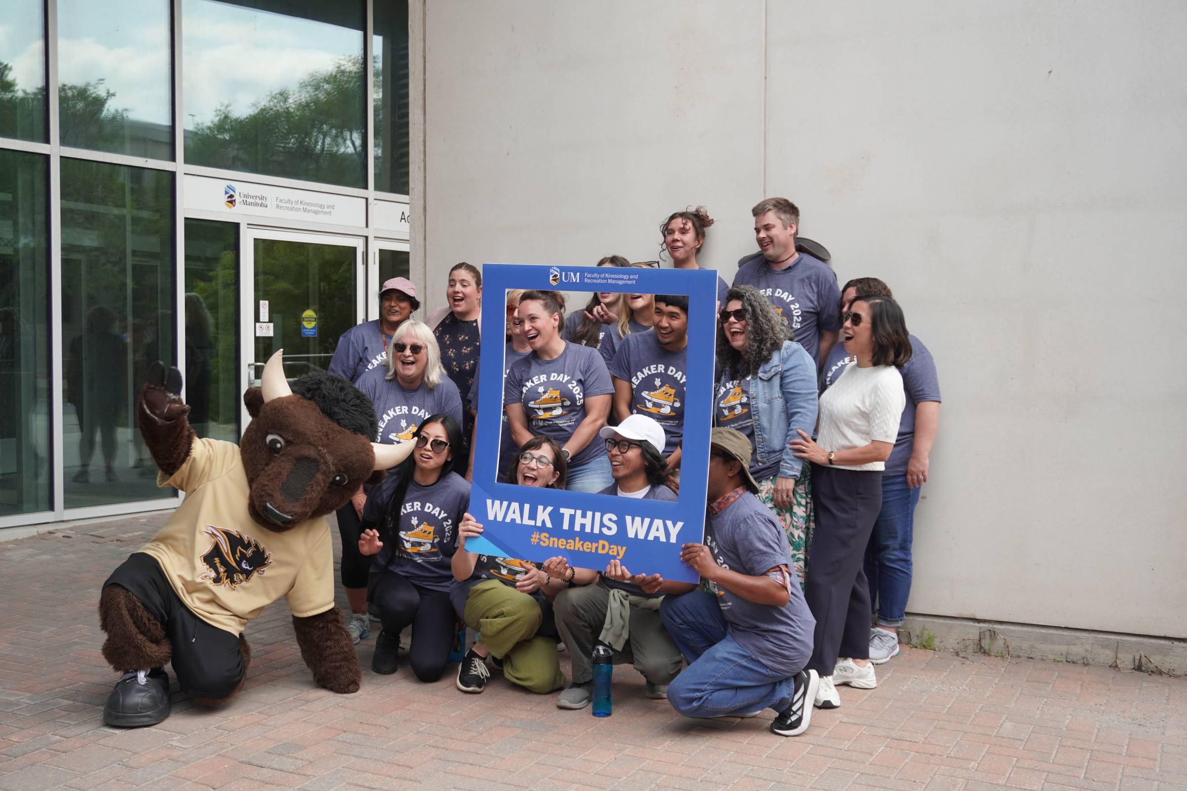 A group of people pose with Billy the Bison and a sign board reading "walk your way"
