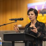 lawyer Marie Henein stands at a podium speaking into a mic with the Faculty of Law banner and moot courtroom art behind her. She is speaking and gesturing with her hands. Photo by Adam Dolman.
