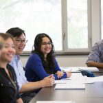 Students smiling at a table, attend an interactive employer information session in Career Services classroom.
