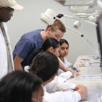Two instructors guide students in a dentistry lab as they examine dental models.
