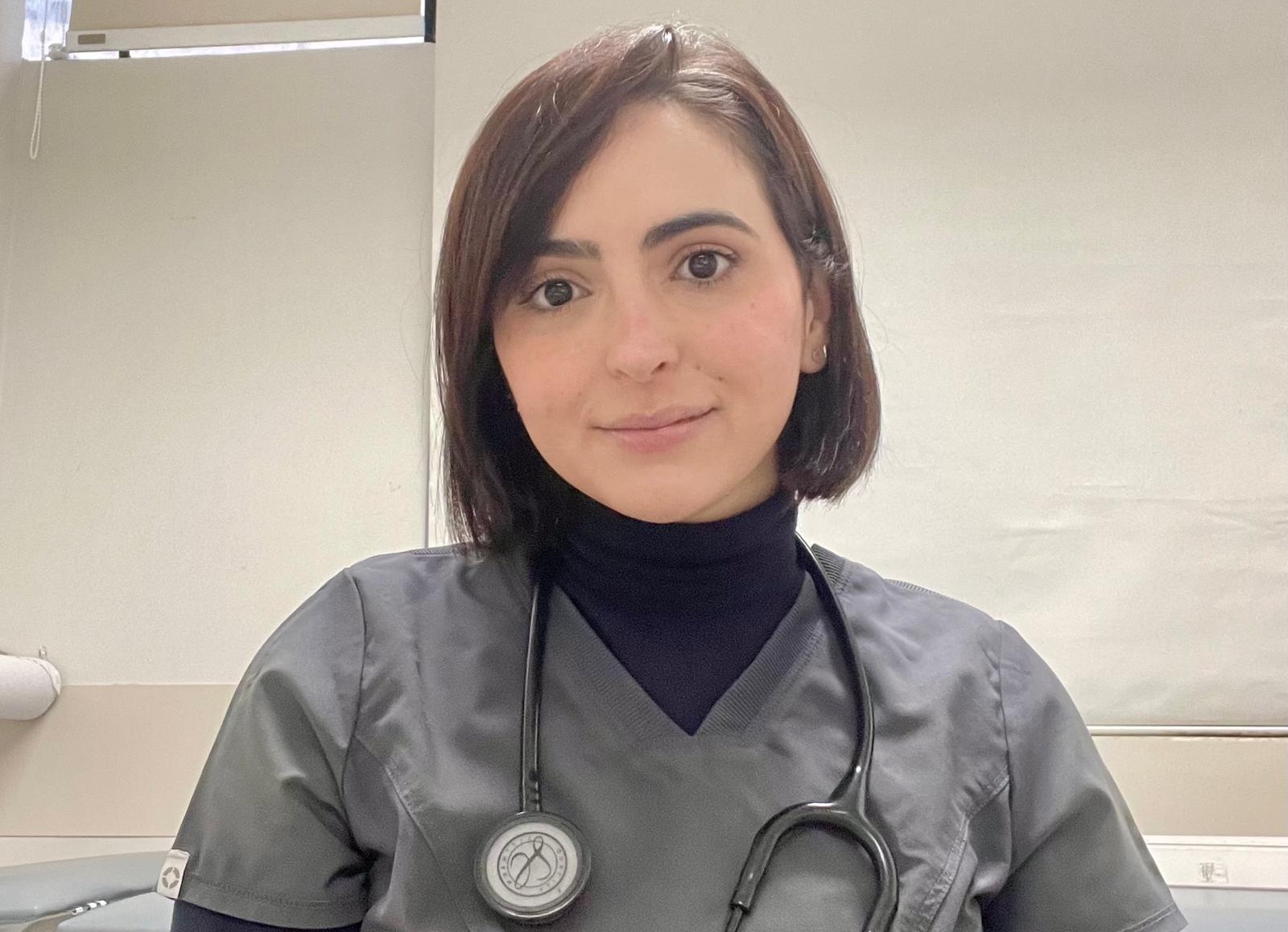 Headshot of smiling medical doctor in grey scrubs with black stethoscope around her neck