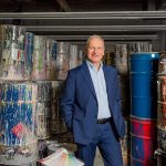 Rick Duha smiling, standing in front of paint drums