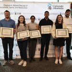 A group of graduate students are posing for a photo while holding their certificate.