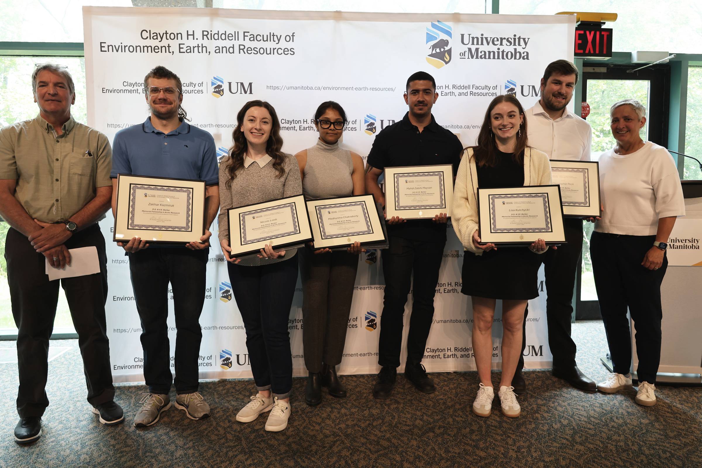 A group of graduate students are posing for a photo while holding their certificate.