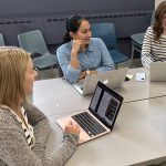 three students sitting at table with laptops