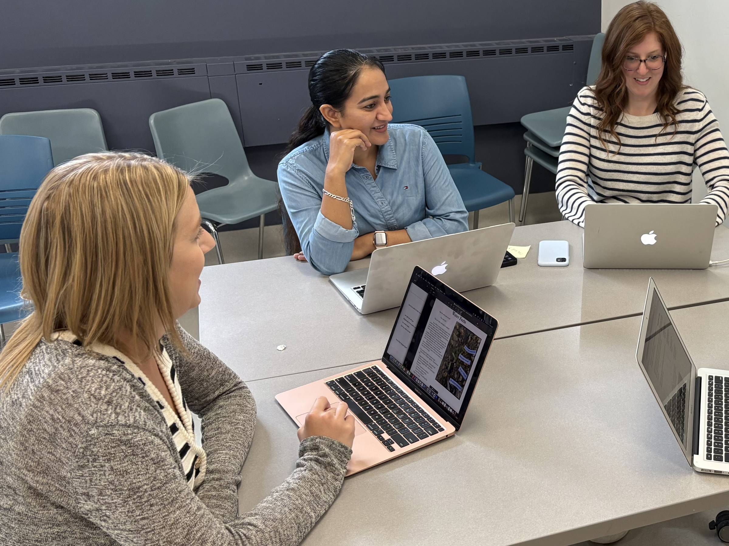 three students sitting at table with laptops