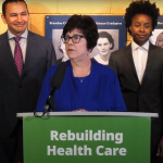 Dr. Joanne Maier speaking at a podium with government officials behind her.