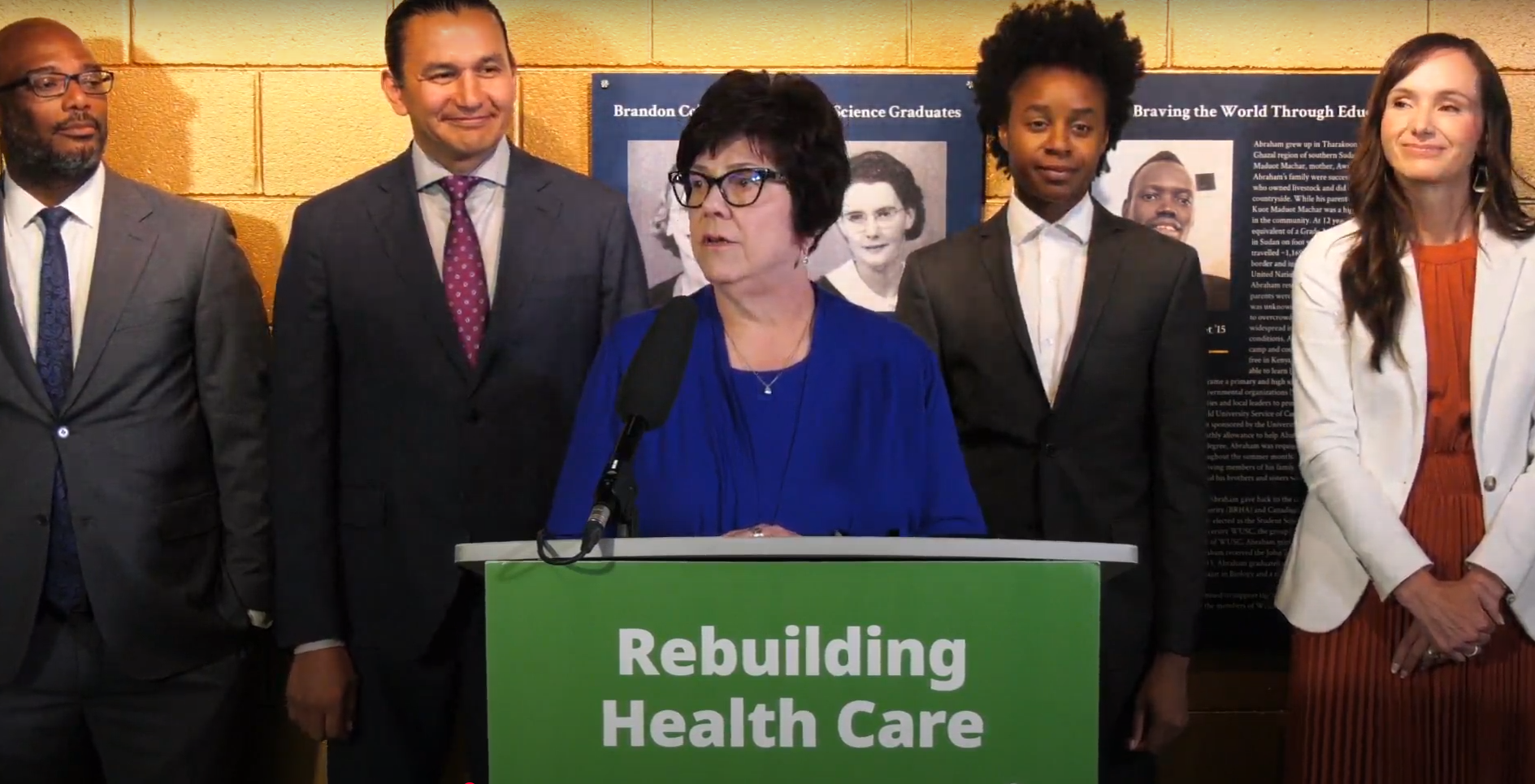 Dr. Joanne Maier speaking at a podium with government officials behind her.